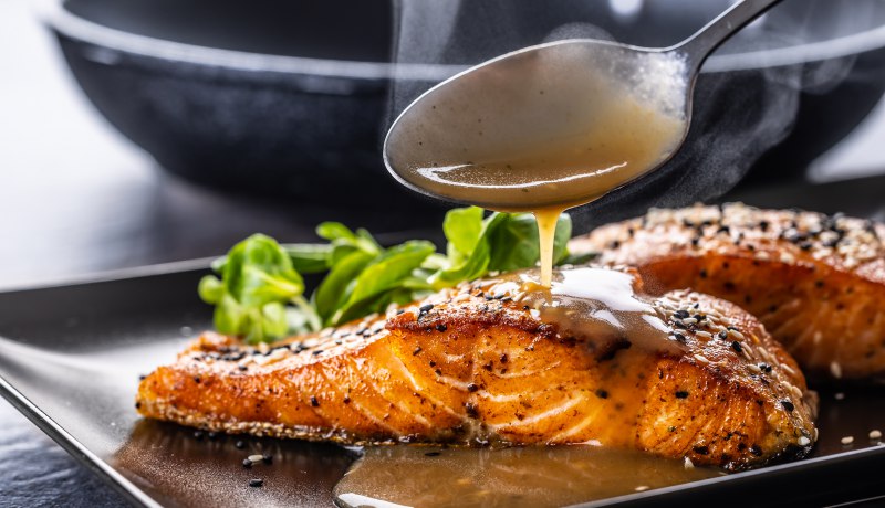 spoon finishes portion by pouring demiglas sauce salmon fillets